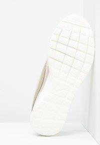 Nike-tossua, jossa on valkoinen kumipohja, jossa on teksturoitu pito. Yläosa on beigea nubukkinahkaa, jossa on sulava, virtaviivainen muotoilu.