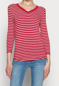 Punavalkoraidallinen pitkähihainen V-kaula-aukkoinen paita, jossa istuva malli ja joustava kangas. Päällä on hillitty logo lähellä rintaa ja resorit hihansuissa.