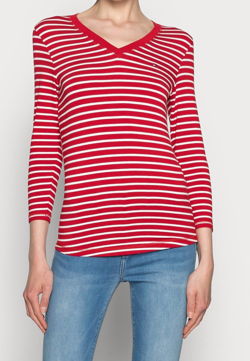 Punavalkoraidallinen pitkähihainen V-kaula-aukkoinen paita, jossa istuva malli ja joustava kangas. Päällä on hillitty logo lähellä rintaa ja resorit hihansuissa.