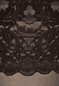 Sort blonde stof med blomster mønstre og intrikate detaljer, lagdelt over en nude tekstur, hvilket skaber et delikat og struktureret udseende.