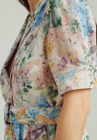 Abito floreale realizzato in un tessuto leggero con motivi vibranti di rosa, blu e verde. Il design include maniche corte e un accentuato con una cintura.