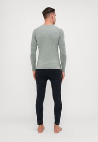 Camisola justa de mangas longas em tecido canelado verde claro, combinada com calças slim pretas. Design simples com mínimos detalhes, sem hardware visível.