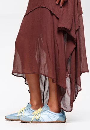 Sneaker blu e azzurri con lacci gialli, abbinati a un vestito borgogna fluido e trasparente con un design a strati e un orlo ondulato.