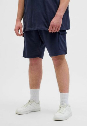 Pantaloni corti blu navy con tasca laterale, realizzati in tessuto morbido. Abbinati a sneakers bianche e calzini bianchi rigati coordinati.
