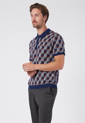 Polo de punto en azul marino, rojo y gris con un patrón geométrico, que presenta un cuello, mangas cortas y detalle de ribete en el dobladillo.