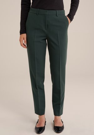 Pantalons taillés vert foncé avec une coupe slim, devant plat et deux poches latérales, associés à des ballerines noires, sur un fond neutre.