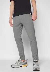 Gray, textured pants with a tailored fit, featuring a subtle pattern. Paired with gray sneakers with yellow accents and black laces.