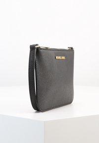 Czarna syntetyczna torebka na ramię o teksturowanej powierzchni, zamknięciu na zamek i złotym logo z przodu. Posiada odpinany pasek.