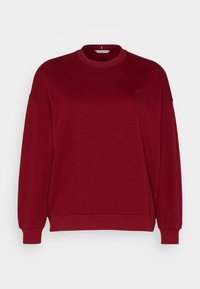Sweatshirt bordeaux avec col rond, épaules tombantes, poignets et ourlet côtelés, arborant un logo en relief subtil sur la poitrine.