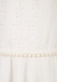 Bílá látka se vzorem zlatých teček a lemováním z perlových korálků na okraji. Měkká textura, plynulý design.