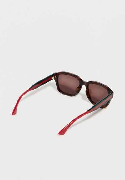 Lunettes de soleil carrées écaille de tortue avec verres marron, branches vertes et rouges, et détail logo doré sur les branches.