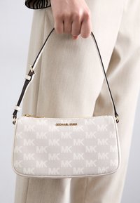 Borsa a tracolla bianca in tela con motivo MK discreto, cerniera dorata e tracolla regolabile marrone. Forma quadrata e texture liscia con dettaglio del logo.