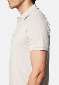 Jasno beżowa koszulka polo z teksturowanej tkaniny, klasycznym kołnierzykiem, zapięciem na guziki i krótkimi rękawami.
