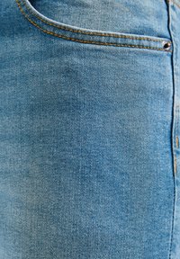 Světle modrá denimová látka s jemnou strukturou, obsahující přední kapsu a oranžové stehy podél švů.