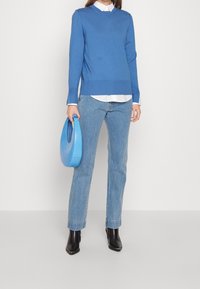 Blå tröja med ribbad nederkant, bärs över en vit skjorta med krage. Ljusblå handväska, raka denimjeans och svarta spetsiga ankelstövlar.