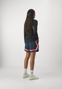 Must nad käised, sinised lühikesed püksid punase ja valge äärisega, valged sokid ja valged tennisetossud, vaadatuna tagant, minimaalse taustaga.