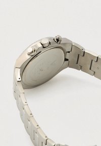 Relógio cronógrafo em aço inoxidável com acabamento escovado; possui três botões e uma pulseira sólida; fundo da caixa arredondado liso com detalhes gravados.