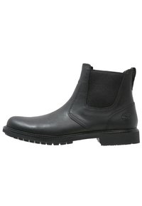 Botín Chelsea de cuero negro con paneles laterales elásticos, punta redonda y suela de goma texturizada. Presenta un logotipo en el talón.