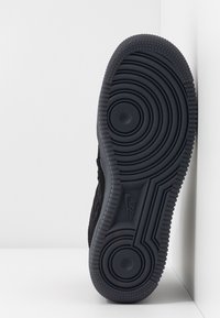Semelle de sneaker en caoutchouc noir avec un motif texturé, des cercles concentriques et des accents en relief. Logo visible sur le côté.