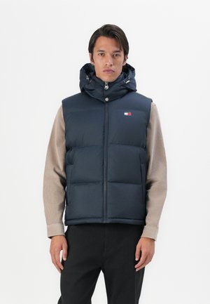 Navy blue padded vest with a hood, zip closure, front pockets, and a logo patch. Fabric appears smooth and slightly glossy.