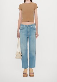 Světle modré džíny s rovnými nohavicemi, hnědý žebrovaný krátký top, béžové sandály na platformě a malá pletená kabelka s krátkými poutky.