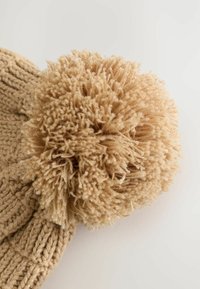 Strik en beige hue med en stor, struktureret tan pom-pom på toppen. Hatten har ribbet detaljer og en blød, fuzzy finish.