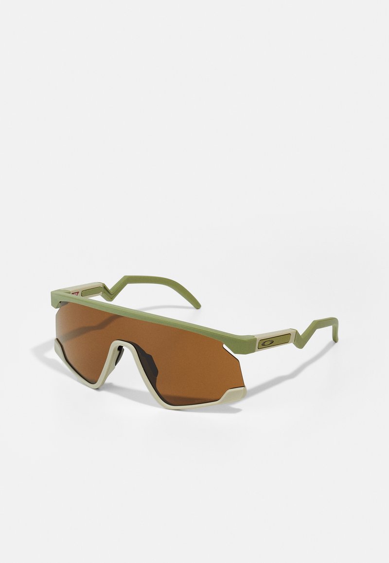 Grün gerahmte Sonnenbrille mit großen braunen Gläsern. Ausgefallenes, eckiges Design, strukturierte Bügel und ein kontrastierender Akzent im Rahmen.