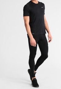 T-shirt de performance noir à manches courtes avec logo Nike réfléchissant, associé à un legging noir ajusté avec un accent réfléchissant. Chaussures de sport noires.