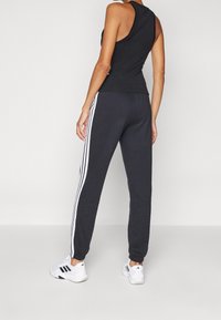 Czarny top na ramiączkach i ciemnoszare spodnie dresowe z białymi paskami po bokach. Do stroju dobrano białe buty sportowe z czarnymi akcentami.