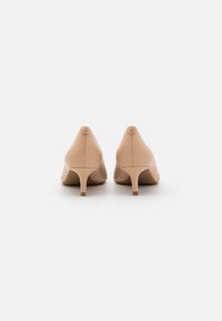 Escarpins en cuir nude à bout pointu et petit talon, avec un accent de bouton logo doré à l'arrière de chaque chaussure.