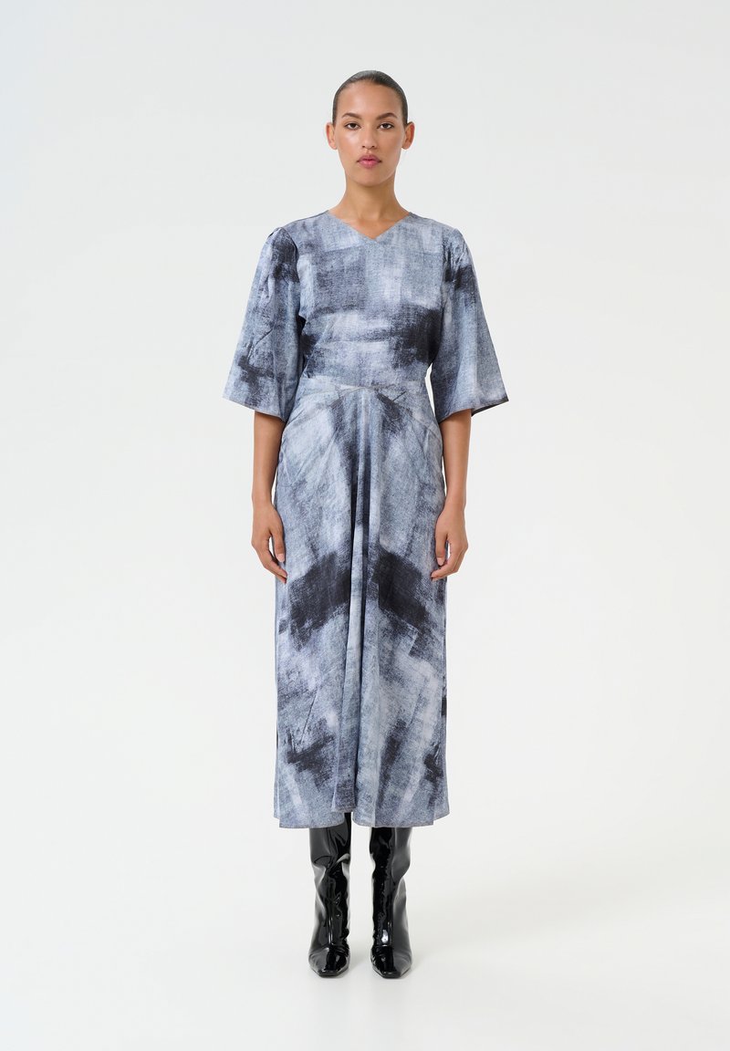Vestito astratto grigio e nero, scollatura a V, maniche a tre quarti, design fluido, abbinato a stivali neri lucidi fino al ginocchio.