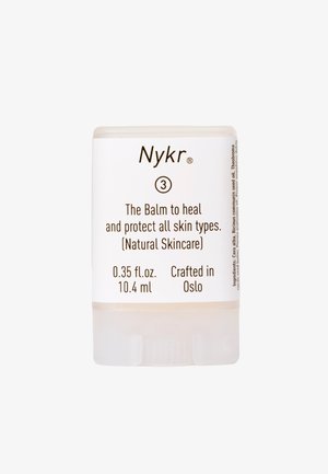 Hvit sylinderformet beholder for balsam med brun tekst, 0,35 fl. oz. kapasitet, merket "Nyk" og "The Balm to heal and protect all skin types."