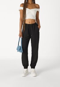 Black jogger pants with elastic cuffs and gold drawstring, paired with a white off-shoulder crop top and a light blue handbag. White sneakers complete the outfit.