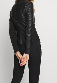 Svart läderjacka med åtsittande design, hög krage och långa ärmar. Har diskreta sömnadsdetaljer och en jämn, glänsande yta.