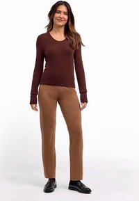 Braunes langärmeliges, geripptes Oberteil, kombiniert mit hellbraunen, gerade geschnittenen Hosen aus weichem Stoff, mit rundem Ausschnitt und minimalen Details.