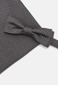 Szary muszka w wzory z małymi czarnymi kropkami, wykonana z teksturowanej tkaniny, umieszczona na tle z pasującej tkaniny. Czyste, ostre krawędzie.
