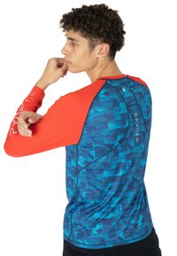 Langärmliges Sporthemd mit einem rot-blauen geometrischen Muster. Besteht aus einem blauen Körper mit roten Ärmeln und Spyder-Branding auf der Rückseite.