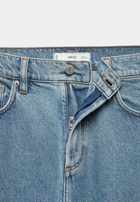 Jean en denim bleu clair avec braguette partiellement ouverte, bouton métallique marqué "MNG" et étiquette de marque visible à l’intérieur de la ceinture.