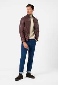 Brun läderjacka med hög krage, dragkedjestängning och sidofickor. Matchas med en krämfärgad turtleneck, blå jeans och mörka ankelstövlar.