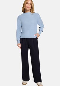 Pull en tricot bleu clair à côtes avec manches longues, encolure ronde et poches latérales ; assorti à un pantalon large noir et des baskets blanches.