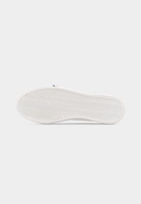 Λευκή σόλα αθλητικού παπουτσιού με μοτίβο διάτρησης ψαροκόκαλου, εμφανιζόμενη από κάτω σε απλό ανοιχτό φόντο.