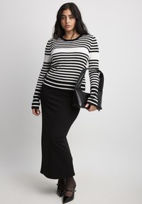 Black and white striped ribbed sweater, paired with a black fitted skirt and a black tote bag. The outfit features long sleeves and a clean silhouette.