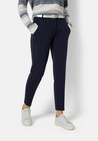 Pantaloni navy con un design sartorial, dotati di tasche laterali e una vestibilità slim. Abbinati a sneakers bianche e a un maglione a righe in maglia.