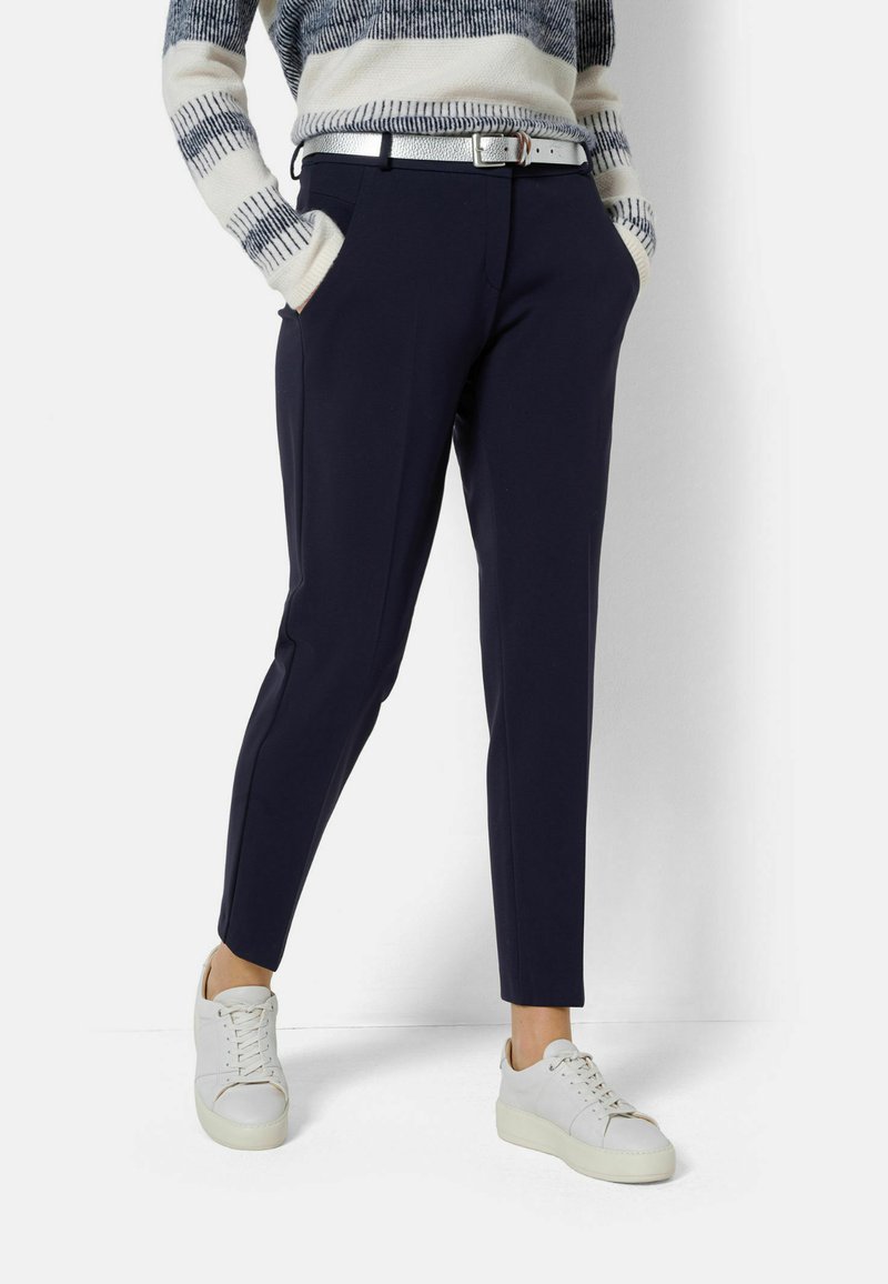 Pantaloni navy con un design sartorial, dotati di tasche laterali e una vestibilità slim. Abbinati a sneakers bianche e a un maglione a righe in maglia.