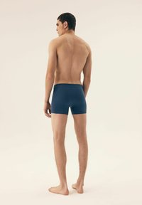 Ciemnoniebieskie bokserki z elastycznego materiału, z miękkim paskiem w talii. Model jest widoczny z tyłu, stojąc na bosych stopach.