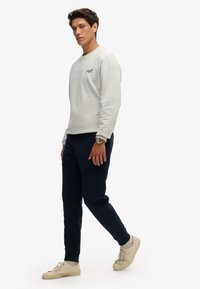 Lichtgrijze sweatshirt met ronde hals en logo, gecombineerd met marineblauwe joggingsbroek en beige sneakers, uitgevoerd in textuurstof en met een aansluitend ontwerp.