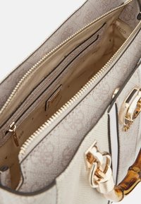 Jasno beżowa torebka z teksturowanym wykończeniem, złotymi akcentami i drewnianym uchwytem. Wnętrze posiada liczne kieszenie i suwaki.