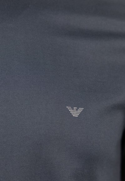 T-shirt bleu foncé en coton lisse avec un petit logo d'aigle argenté sur la poitrine gauche, doté d'un col rond et de manches courtes.