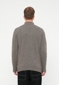 Γκρι πλεκτό πουλόβερ με ψηλό γιακά, ριχτές μανσέτες και ελαφρώς πιο μακρύ πίσω μέρος. Μαλακή υφή και χαλαρή εφαρμογή. Καθαρός, απλός σχεδιασμός.