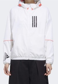 Hvid zippered jakke med hætte, prydet med tre sorte striber på brystet og røde detaljer, lavet af glat, letvægtsmateriale, elastisk talje.